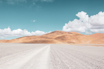 Camino de tierra blanca en paisaje desértico con montañas suaves y cielo con nubes esponjosas