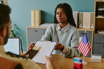African American woman holding clipboard and pen during visa interview. Office setting with...