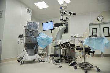 Empty operating room featuring advanced surgical microscope, medical monitors, and covered operating table, showcasing modern equipment prepared for upcoming medical procedure