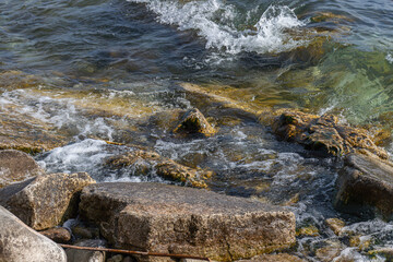Clear lake water splashes over mossy rocks and stones on a rugged shoreline, capturing natural textures and motion.