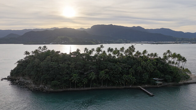 Imagem a&eacute;rea do p&ocirc;r do sol iluminando a Ilha das Cabras em Ilhabela, com c&eacute;u alaranjado e mar calmo ao entardecer
