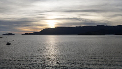 Visão aérea do pôr do sol no Oceano Atlântico em Ilhabela, com reflexos dourados sobre o mar calmo e horizonte tropical.