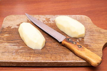 Potato peeling on a wooden cutting board with a knife ready for cooking preparation