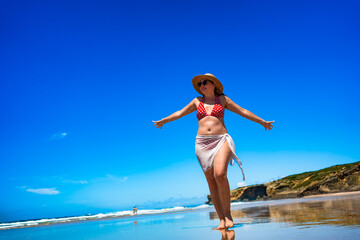 Beautiful mid adult woman model walking on sandy beach in summertime. Front view. Monte Clerigo beach on Algarve coast in Portugal