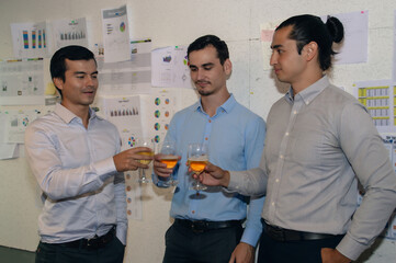 Three professionals celebrating success with drinks in a modern office environment, showcasing...
