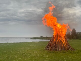 Midsummer bonfire burning in forest by lake on a misty evening