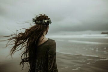 Woman with floral crown gazes at ocean with windswept hair on cloudy day at beach