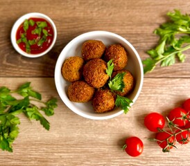 falafel in a plate with tomatoes, herbs and sauce on a wooden background