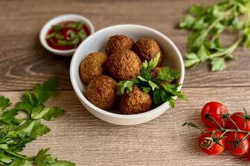 falafel in a plate with tomatoes, herbs and sauce on a wooden background