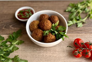 falafel in a plate with tomatoes, herbs and sauce on a wooden background