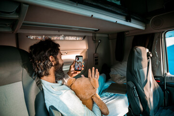 Truck driver video calling family from sleeper cab holding teddy bear