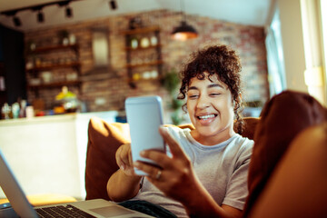 Happy woman listening to music with earphones on phone while relaxing at home