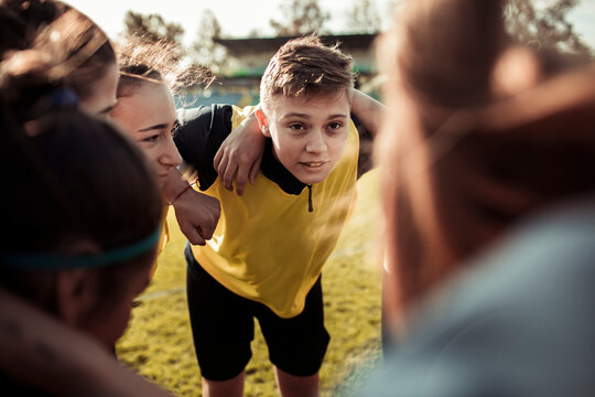 Teen soccer team in yellow jerseys huddling before match on outdoor field