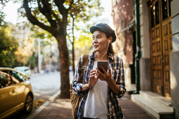 Young woman using a smart phone while walking on the sidewalk in a city
