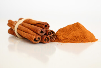 Cinnamon sticks and powder on white reflective background. Selective focus. Macro.
