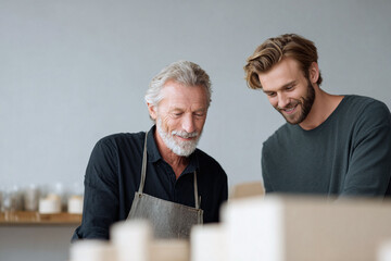 Two men, generations apart, work together, smiling. Father and son, mentorship, or collaboration concept. Crafts, pottery, family business theme.