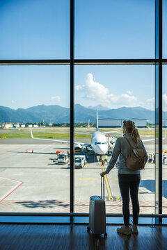 Woman tourist with suitcase waiting at airport terminal before boarding airplane. Solo travel passenger ready for flying to summer vacation