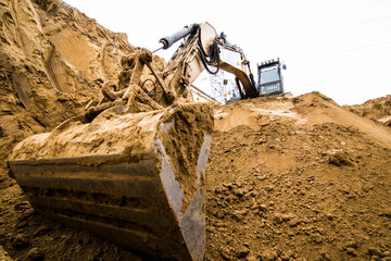 Dramatic low-angle close-up of a powerful excavator's dirty, massive digging bucket positioned...