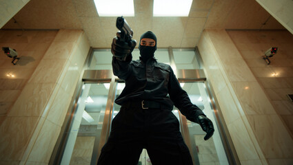 A thief dressed in black with gloves and a ski mask aims a gun while standing in a corridor of a modern building. Security cameras are visible above. Crime and robbery concept. Generative AI.