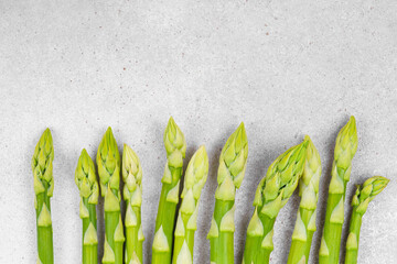 Bunch of raw fresh green asparagus stalks macro, close up on light gray textured background with...