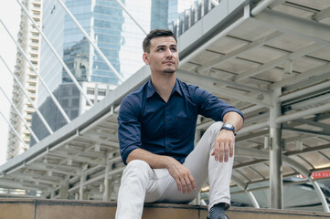 Stylish young man sitting outdoors in an urban setting, reflecting on life and responsibilities.