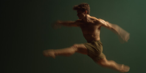 A male dancer leaps gracefully, exhibiting fluidity and athleticism against a solid backdrop. The image captures motion and artistic expression through a skilled performance.