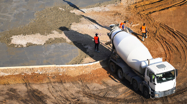 construction workers in safety vests supervising concrete pouring from a cement mixer truck. The freshly poured concrete forms the foundation for a new building or infrastructure project