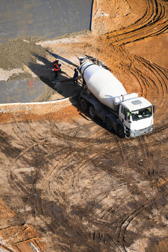 construction workers in safety vests supervising concrete pouring from a cement mixer truck. The freshly poured concrete forms the foundation for a new building or infrastructure project
