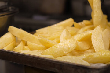 Close-up of raw potato wedges freshly cut and placed in a metal tray, ready for frying in a commercial kitchen setting

