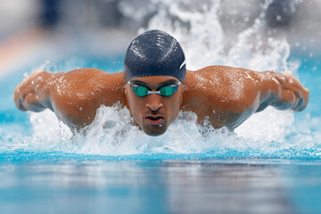 An athlete gracefully swims the butterfly stroke in the pool, his form is perfect and the water splashes