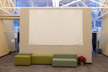 Spacious interior lounge area featuring a large blank white canvas, arranged seating, and ambient lighting, ideal for creative projects, presentations, or relaxing time.