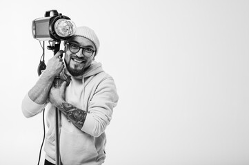 Portrait of a stylish man in hoodie and beanie setting up professional studio lighting equipment....