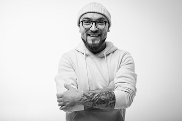 Confident man with crossed arms, wearing a beanie and glasses. Striking black and white studio...