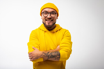 Portrait of a confident young man in a yellow hoodie and cap, with glasses and tattoos on his arms...