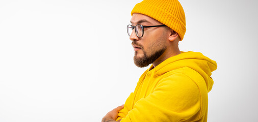 Side view portrait of modern bearded man in yellow hoodie and beanie, arms crossed, standing on...