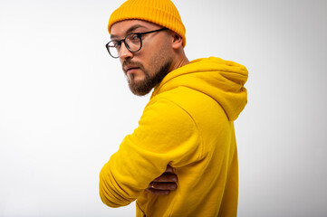 Side view portrait of modern bearded man in yellow hoodie and beanie, arms crossed, standing on...