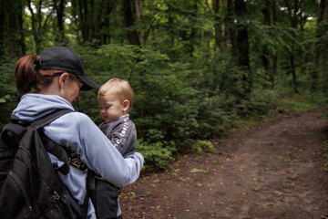 Mother holds baby in baby carrier while traveling through forest. Nature walk with baby, peaceful moment in fresh air, family bonding in forest.