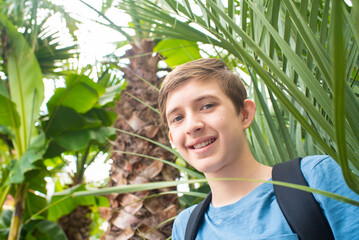 12 year old smiling boy with backpack  under palm trees	