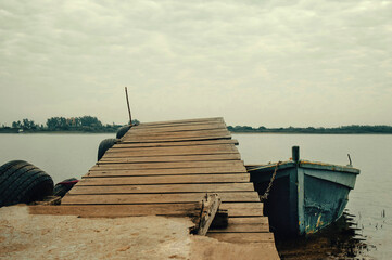 Old wooden pier leading to small moored boat on cloudy day