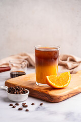 Coffee with orange juice (bumble) in a tall glass with ice on a light background with coffee beans...