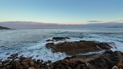 A tranquil and peaceful coastal scene featuring gentle waves lapping against rocky shores beneath a serene sunset sky