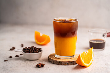 Coffee with orange juice (bumble) in a tall glass with ice on a light background with coffee beans...