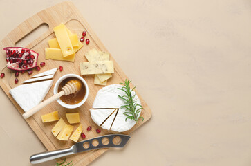 A variety of cheese, honey, pomegranate seeds and rosemary leaves on a wooden board and beige background with copy space. Top view and horizontal format.