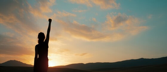 The silhouette of a woman celebrating triumph at sunset with a raised fist