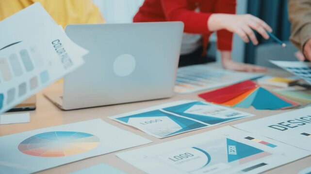 A creative team engages in collaborative design work using a laptop and printed materials, exploring color palettes and mockups in a modern office setting. SACTR