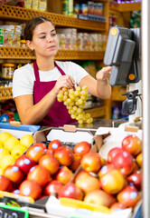 Smiling female shopping assistant weighing grapes in grocery shop