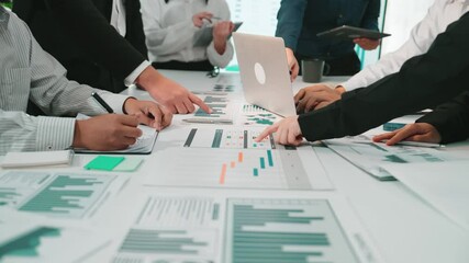 A diverse business team engages in a collaborative meeting, analyzing data displayed on digital screens. Hands gesture over charts, reflecting teamwork in a modern office setting. SACTR - Powered by Adobe