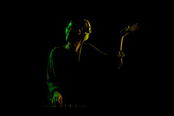 Female DJ with headphones on a mixer. Side lit silhouette of a girl playing techno music against...