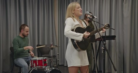 Music band practicing before a concert. A female singer plays guitar and sings, while the drummer and keyboardist accompany her. - Powered by Adobe