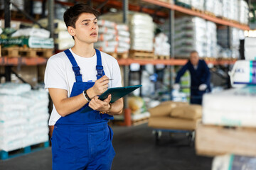 Young man conducts verification, examination and inspection of goods in warehouse and records work...